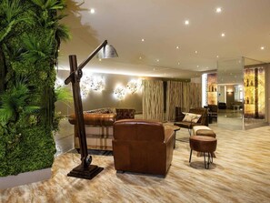 A modern lounge area with a sofa, armchairs, a lamp, and a decorative wall with a vertical garden. - Hôtel Mercure Marseille Centre Vieux-Port (MARSEILLE)
