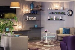 A modern living room with a sofa, a coffee table, a lamp, and decorative items on shelves. - Hôtel Mercure Marseille Centre Vieux-Port (MARSEILLE)