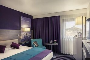 A hotel room with a bed, a desk, a chair, a small table, and a window with curtains. - Hôtel Mercure Marseille Centre Vieux-Port (MARSEILLE)