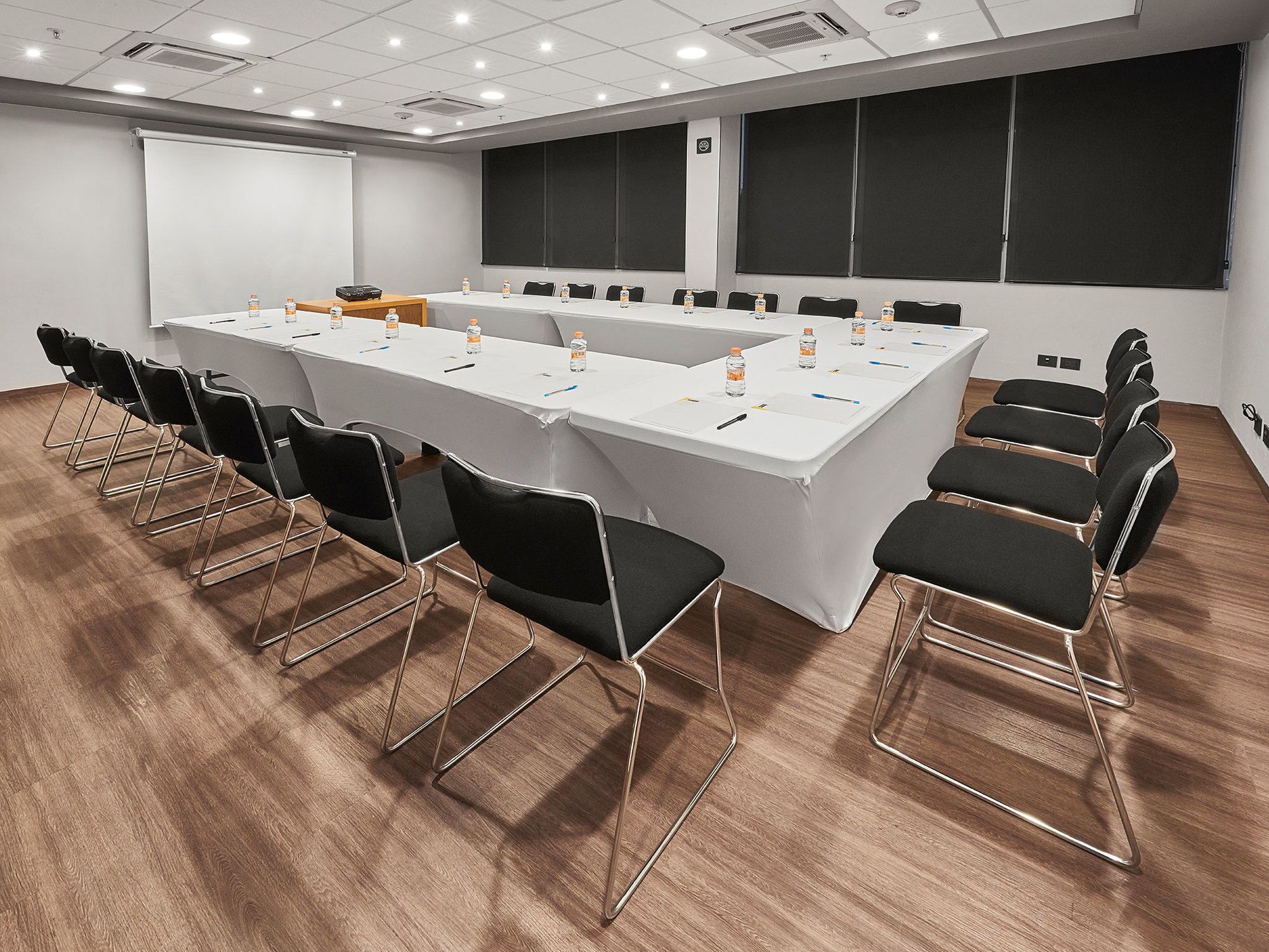 A conference room with a long table, black chairs, and a projector screen.