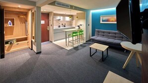 A modern living room with a sofa, a coffee table, a TV, and a kitchen area with a dining table and chairs. - City Express by Marriott Toluca (Toluca)