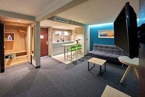 A modern living room with a sofa, a coffee table, a TV, and a kitchen area with a dining table and chairs. - City Express by Marriott Toluca (Toluca)