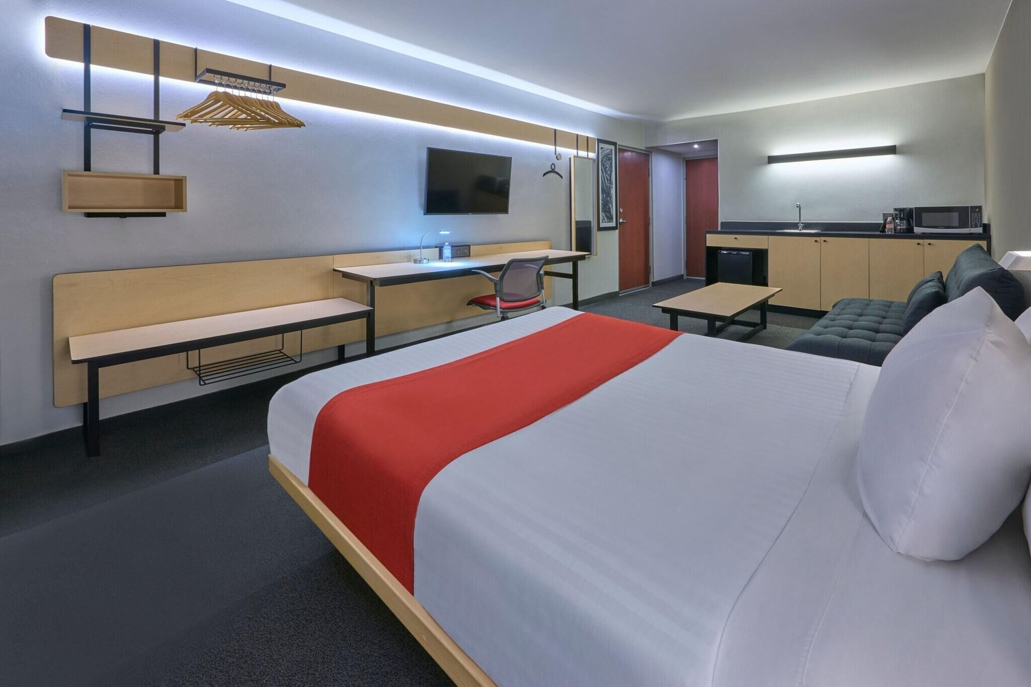 Een hotelkamer met een bed, bureau, stoel, kitchenette en televisie.