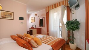 Quarto de hotel com cama, escrivaninha, televisão e planta em vaso.