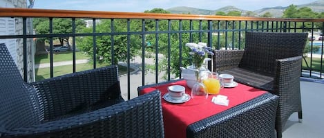 A balcony with wicker furniture, a red tablecloth, and a view of a green landscape.