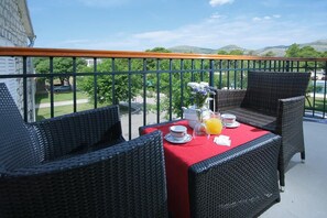 A balcony with wicker furniture, a red tablecloth, and a view of a green landscape. - Trogir (Trogir)