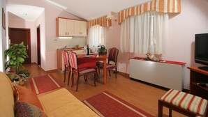 A living room with a sofa, a dining table with chairs, a kitchen area, a TV, and a window with curtains. - Trogir (Trogir)