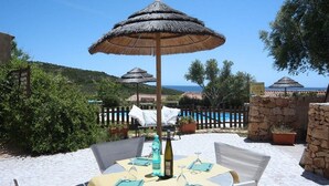 An outdoor dining area with tables, chairs, and thatched umbrellas. - Baia Salinedda (San Teodoro)