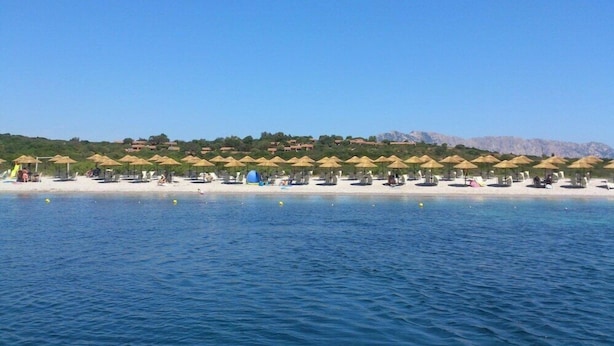 A beach resort with rows of sun umbrellas and lounge chairs along the shoreline. - Baia Salinedda (San Teodoro)