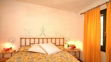 Una camera da letto con una coperta a fiori, una testiera di legno con motivo a forma di albero, due comodini con lampade e una finestra con tende arancioni.