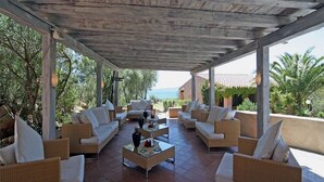 A covered outdoor seating area with wicker furniture and a view of the sea. - Baia Salinedda (San Teodoro)