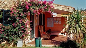 A stone building with a covered porch, a chair, and a map on the wall. - Baia Salinedda (San Teodoro)
