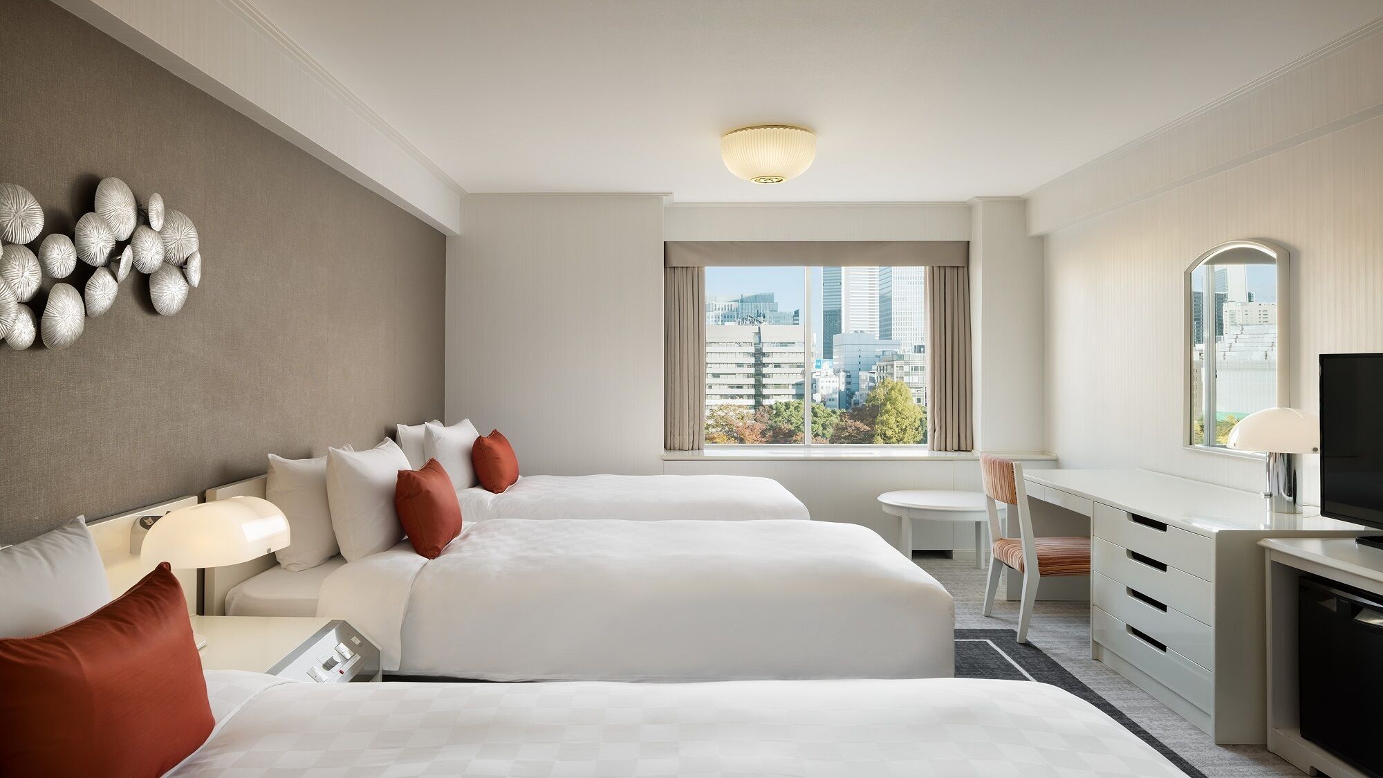 A hotel room with two beds, a desk, a chair, a TV, and a large window with a city view.