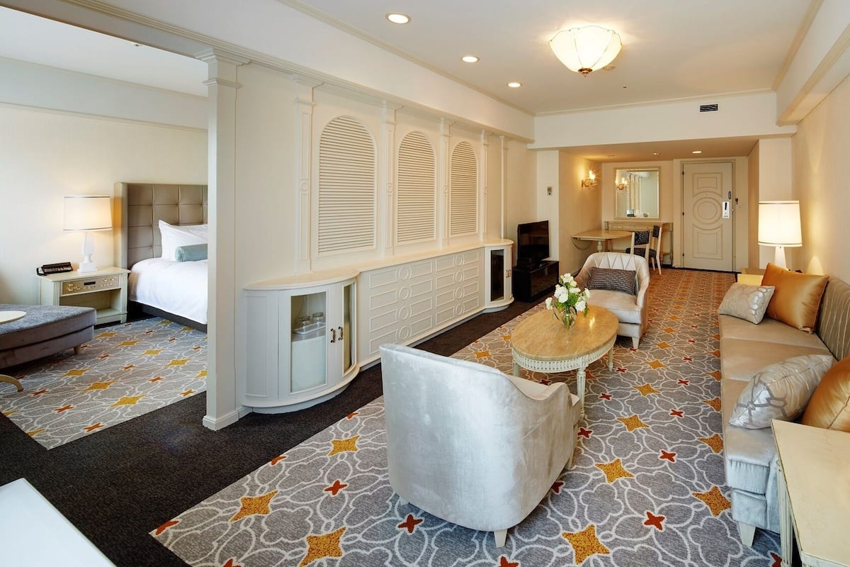 A hotel room with a bed, a sofa, a small table with flowers, a TV, and a mirror.