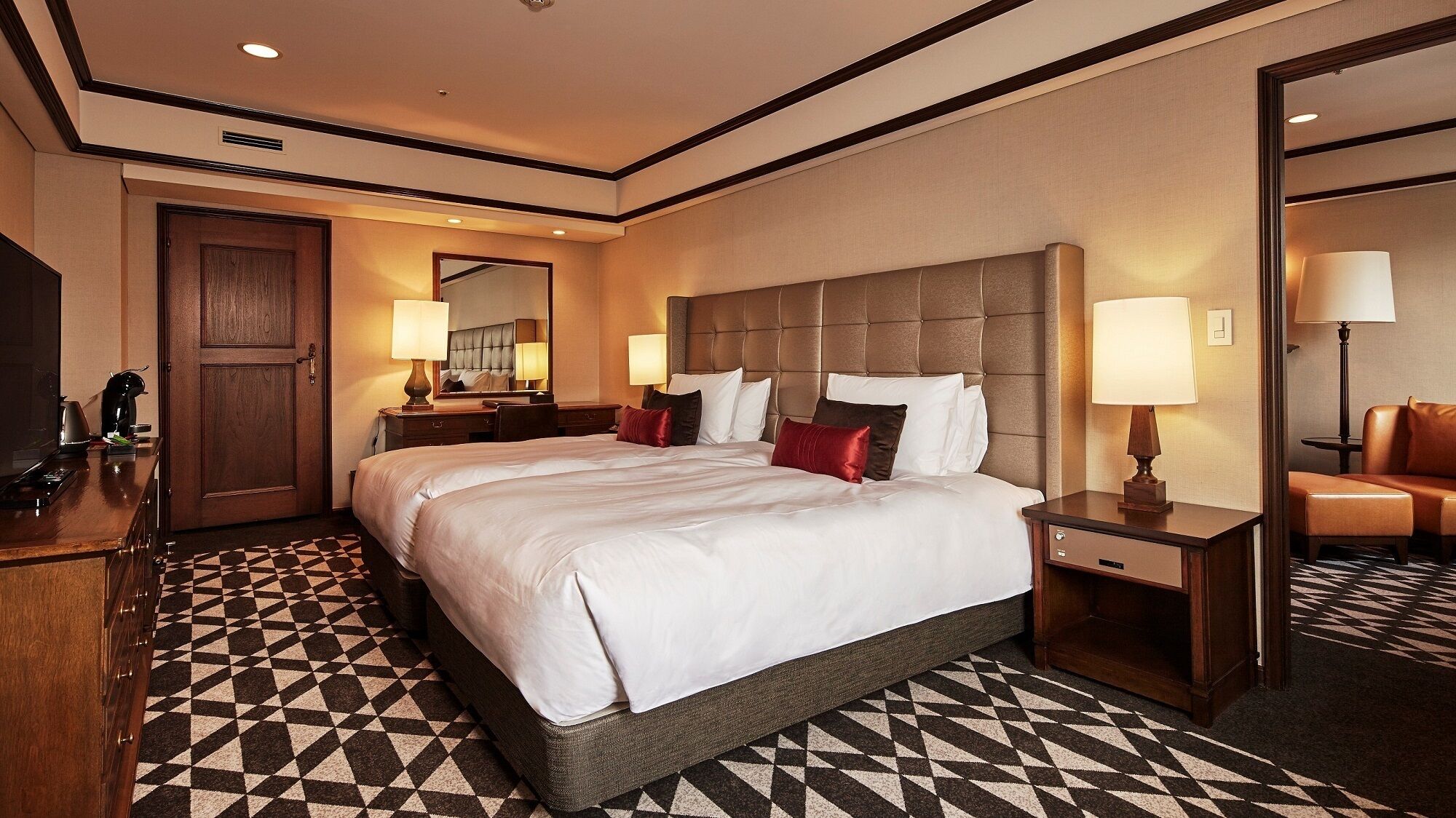 A hotel room with a large bed, a wooden desk, a chair, a dresser, and a mirror.