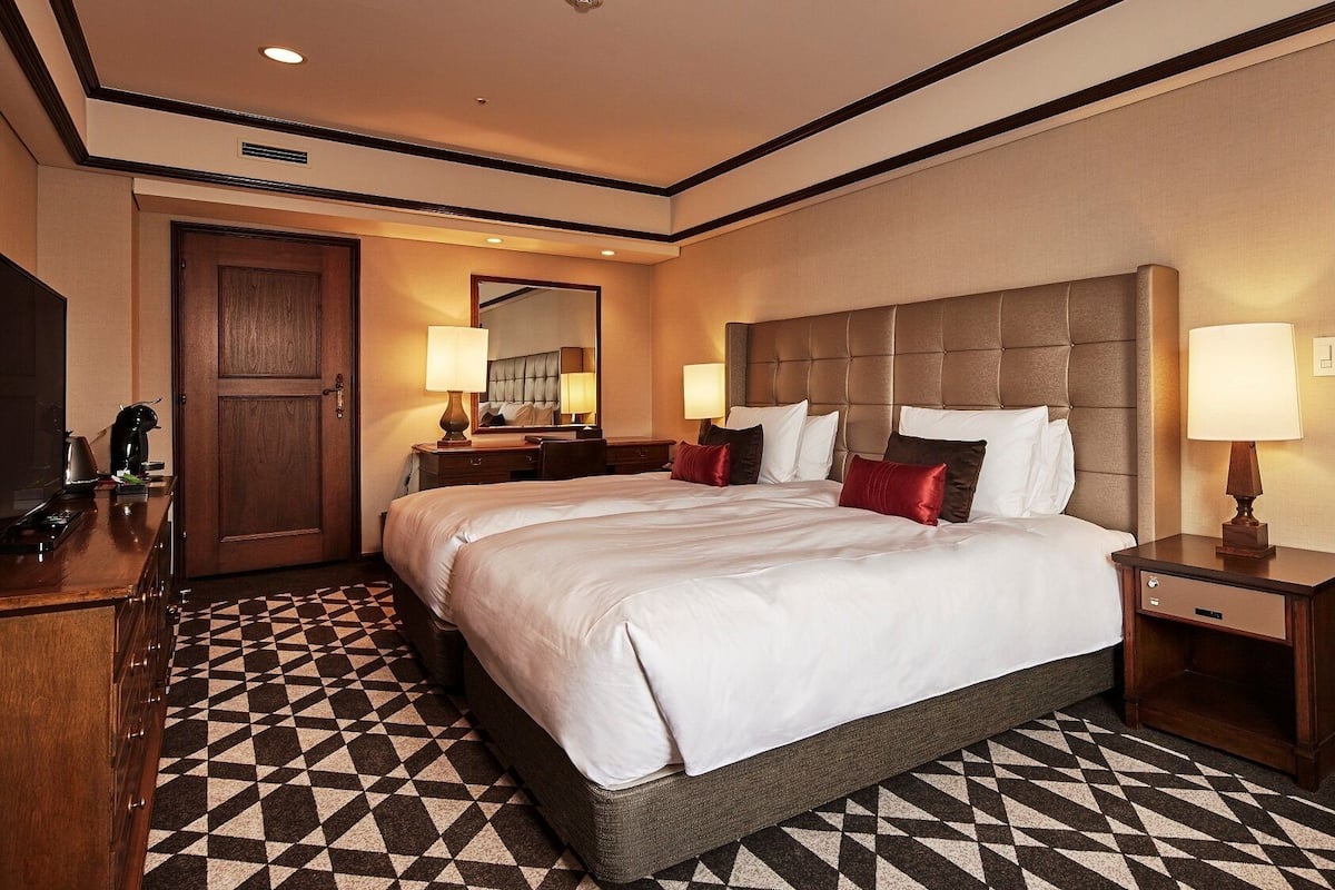A hotel room with a large bed, a wooden desk, a chair, a dresser, and a mirror.