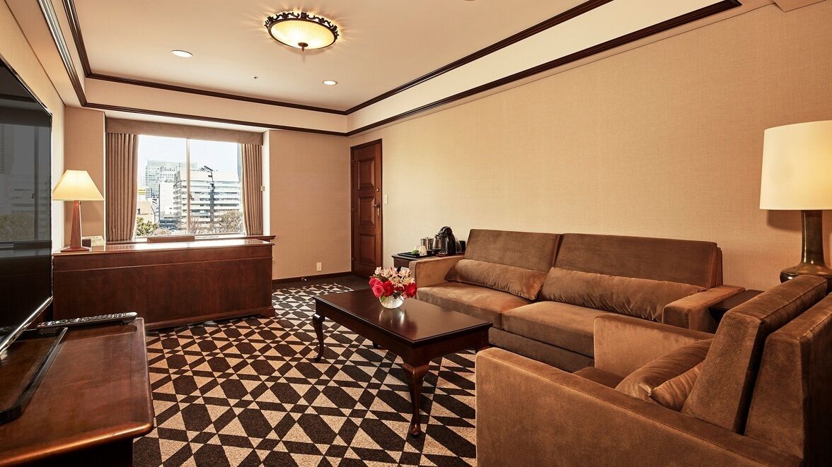 A hotel room with a sofa, a coffee table, a TV, and a patterned floor.