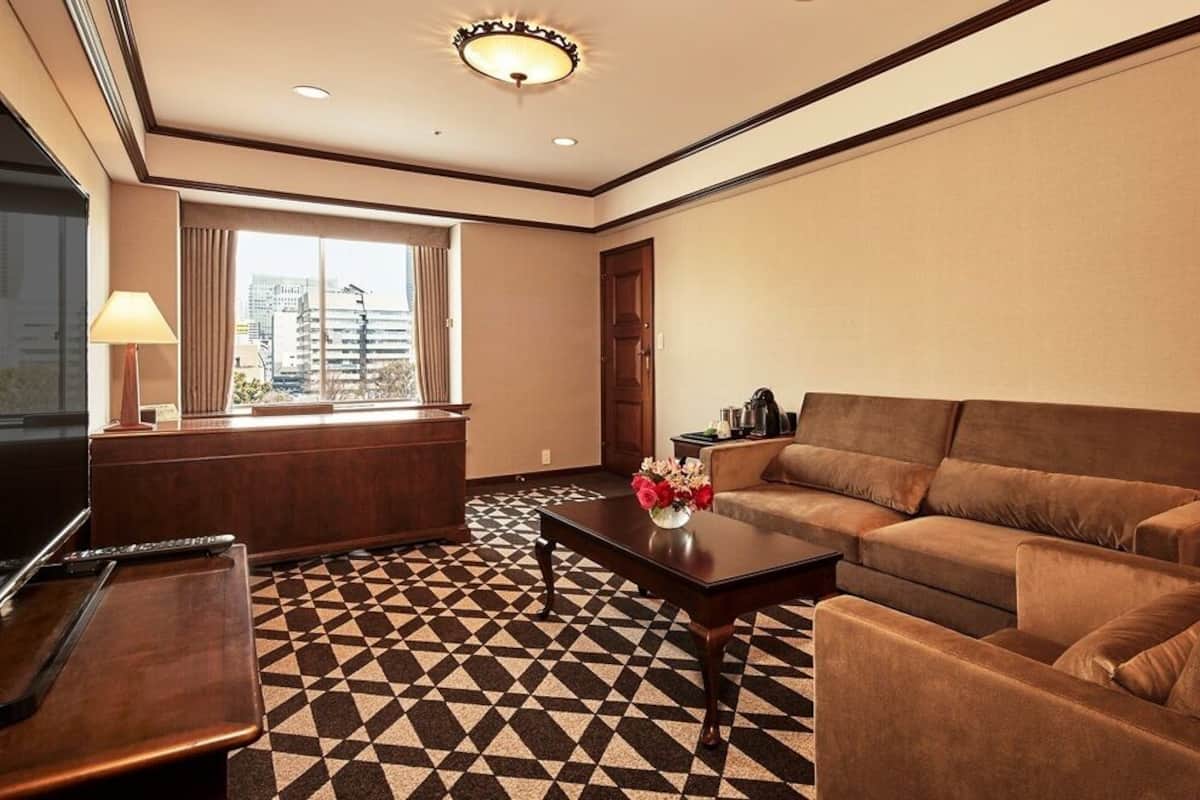 A hotel room with a sofa, a coffee table, a TV, and a patterned floor.
