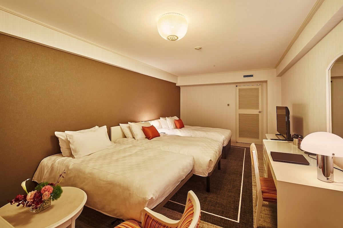 A hotel room with two beds, a desk, a chair, a TV, and a mirror.