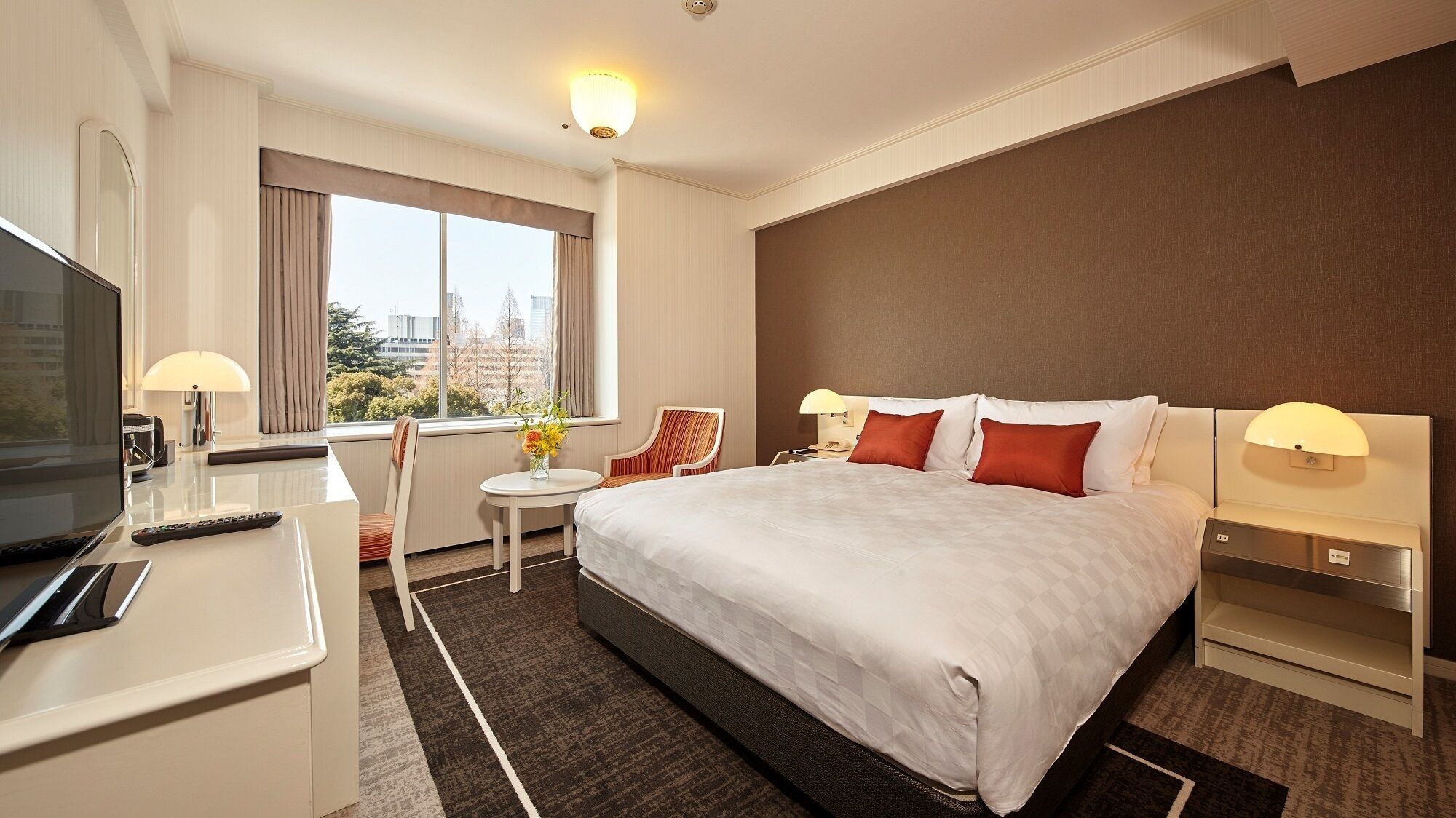 A hotel room with a bed, a desk, a chair, a TV, and a window with a city view.