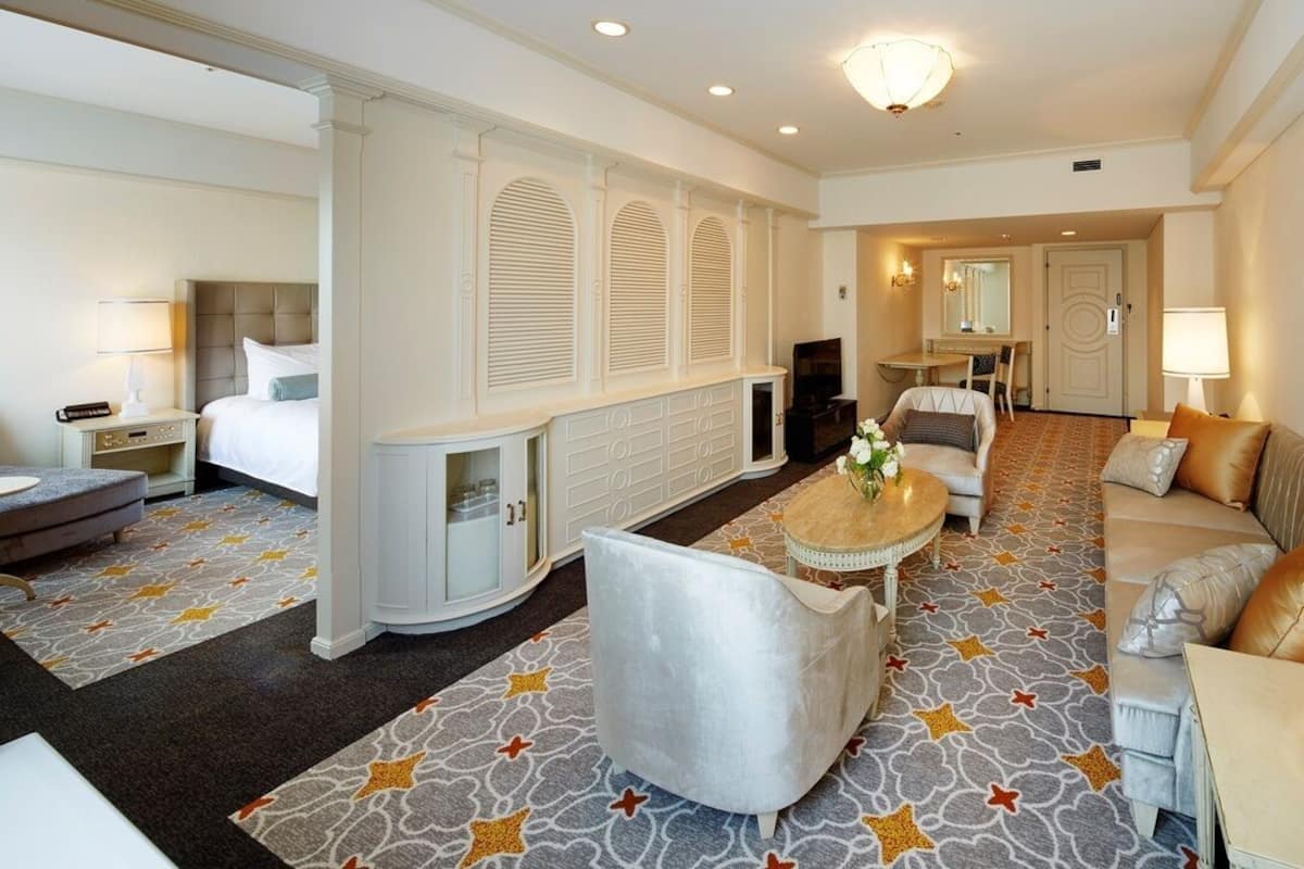 A hotel room with a bed, a sofa, a round coffee table, a TV, and a mirror.