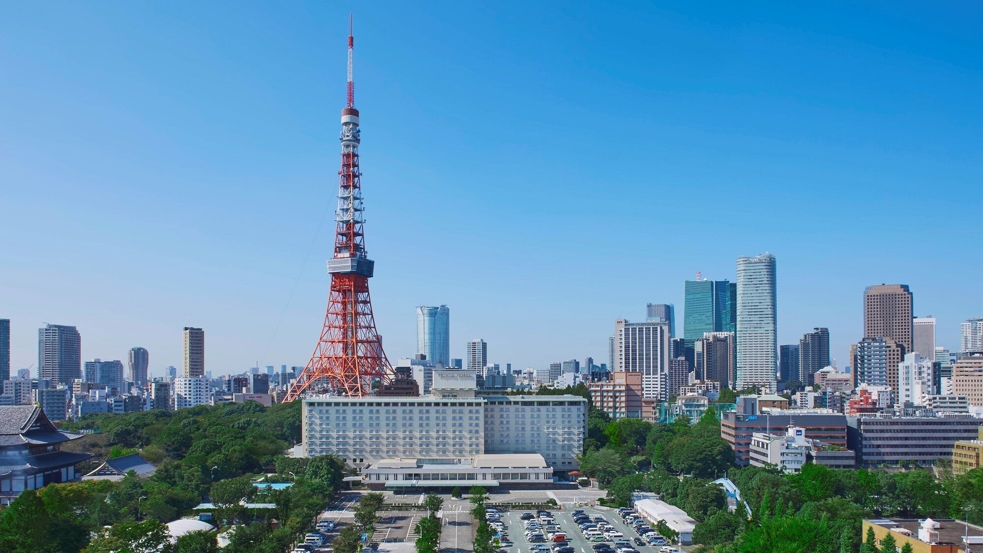 A cityscape with a prominent red tower, modern buildings, and a large parking area.