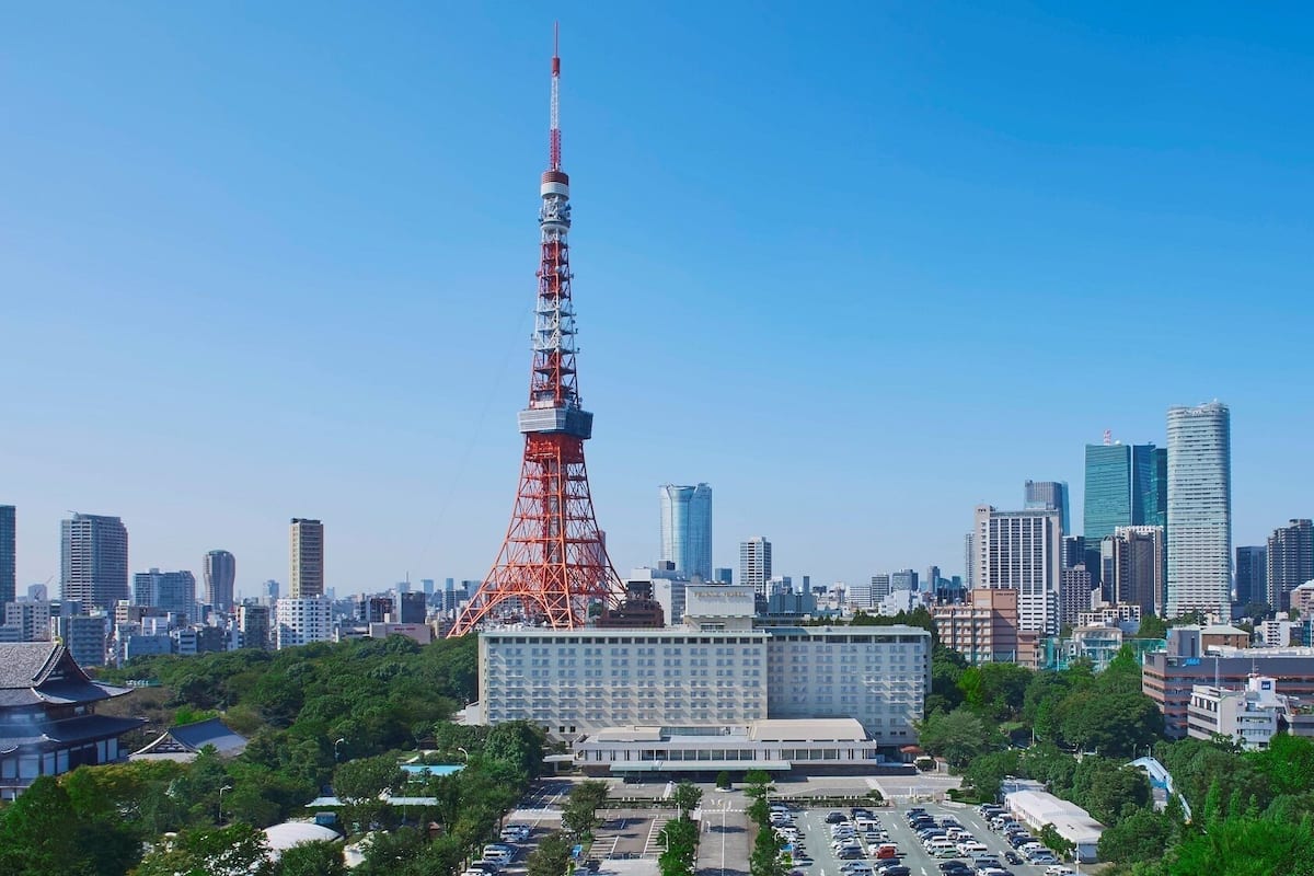 A cityscape with a prominent red tower, modern buildings, and a large parking area.