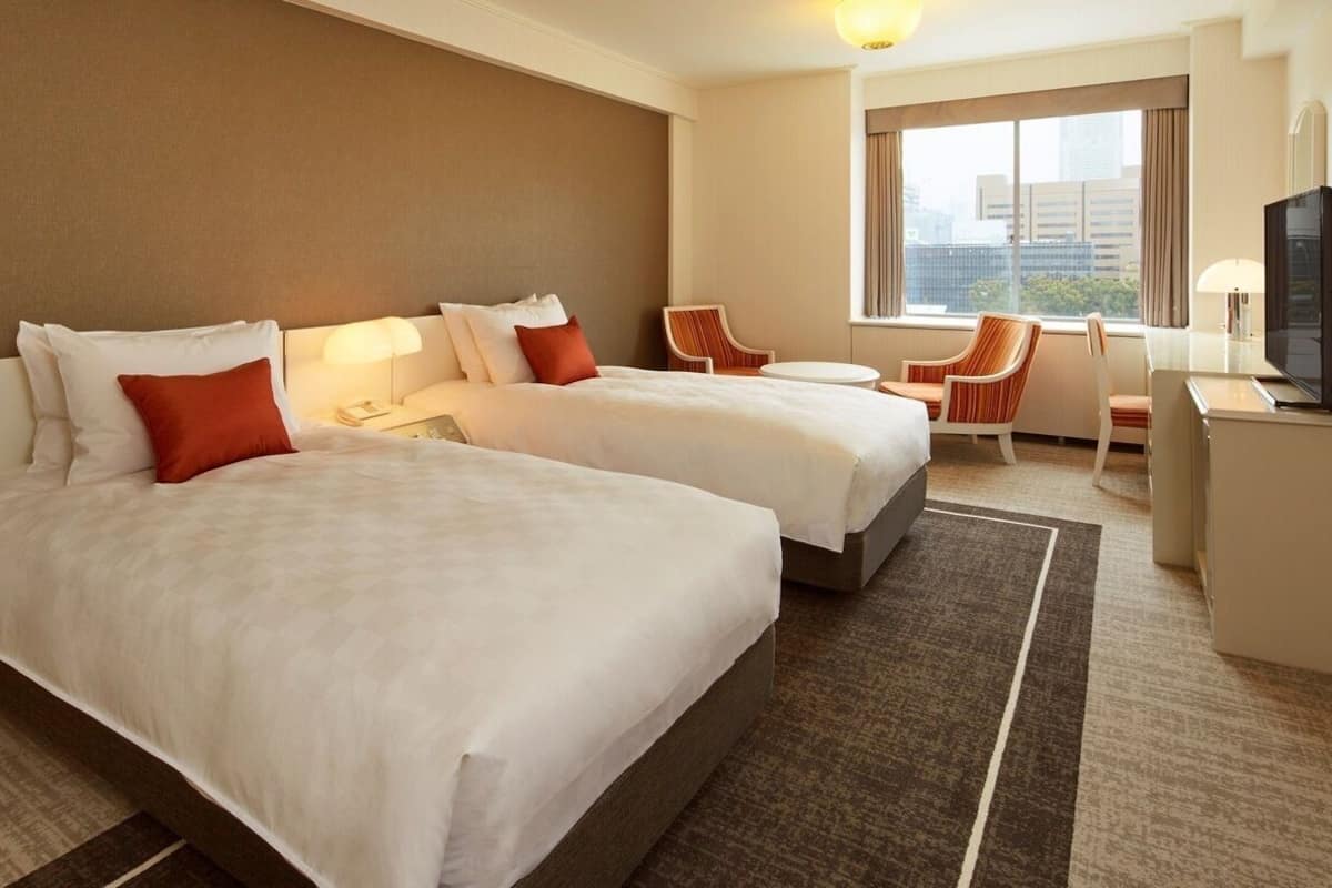 A hotel room with two beds, a desk, a chair, and a TV.