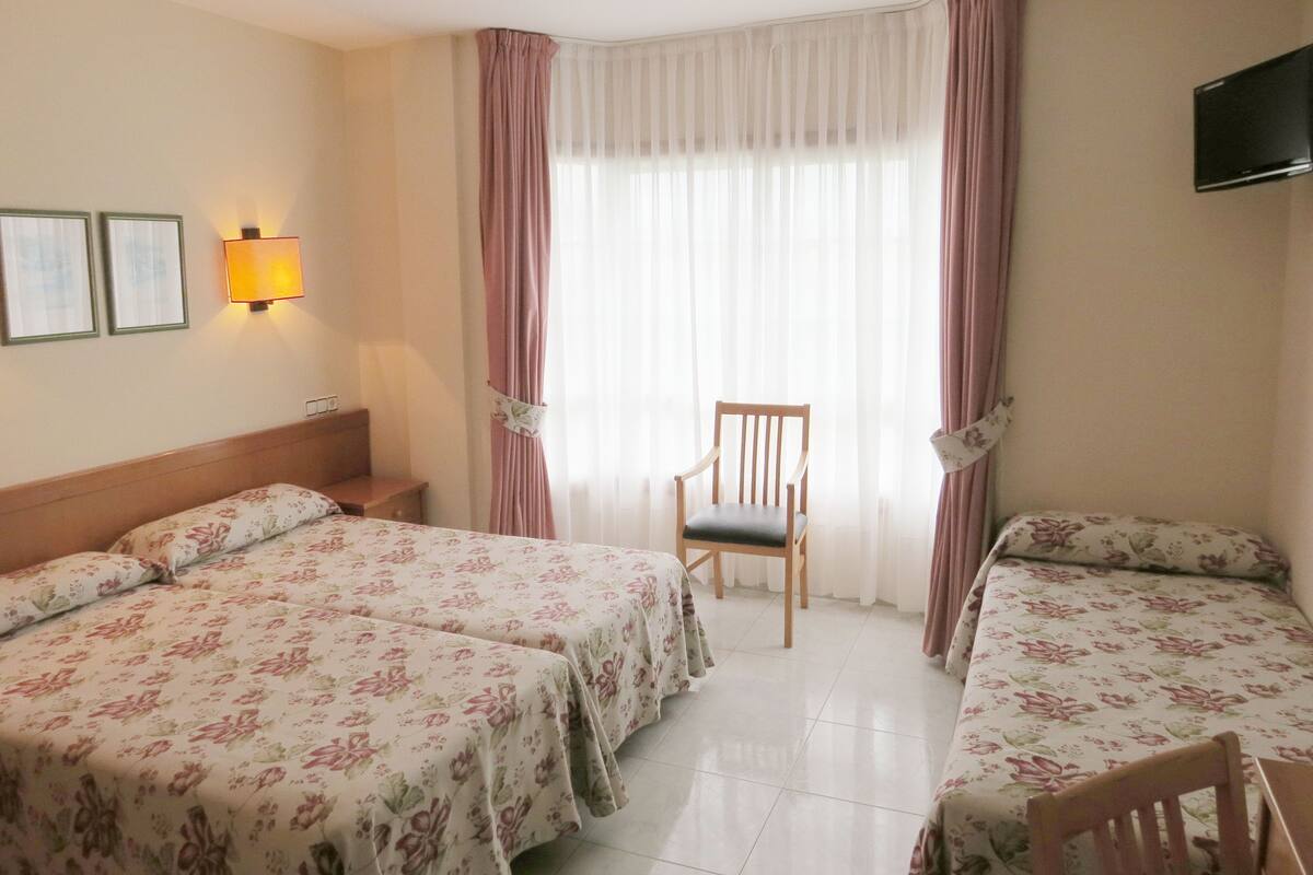 Een hotelkamer met twee bedden, een stoel, een televisie en een raam met gordijnen.
