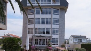 Een hotel met een groot gebouw, een overdekte ingang en een patio met lounge fauteuils.