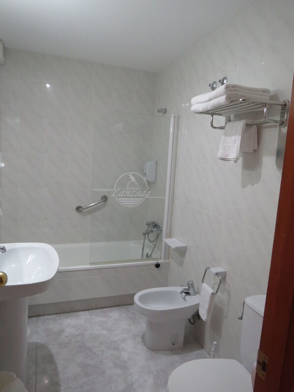 Un baño moderno con ducha de vidrio, lavamanos pedestal, inodoro y bidé.