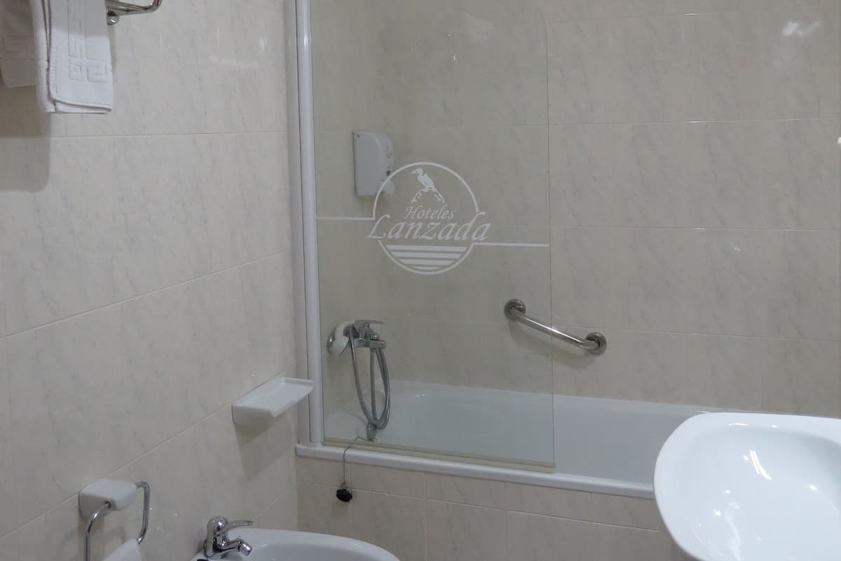 Een moderne badkamer met een douchecabine van glas, een bidet, een wastafel en een handdoekrek met opgevouwen handdoeken.