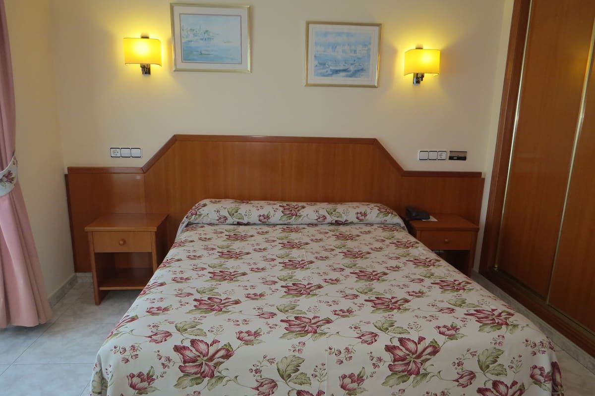 Een netjes ingerichte hotelkamer met een bloemenprint sprei, houten hoofdbord, nachtkastjes en wandlampen.