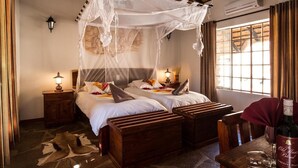 A room with two beds under a canopy, wooden furniture, a stone floor, and a window with curtains. - Canon Village (Fish River Canyon)
