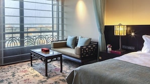 A hotel room with a sofa, a small table, a bed, and a nightstand with a lamp. - Beijing Grand Hotel (Beijing)