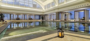 Una amplia piscina cubierta con barrera de cristal, rodeada de zonas de estar y un techo alto con diseño de celosía.