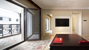 A hotel room with a large window, a flat-screen TV mounted on the wall, a wooden coffee table with a red book, and a patterned carpet. - Beijing Grand Hotel (Beijing)