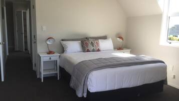 A bedroom with a bed, two bedside tables, a window, and a door leading to another room.