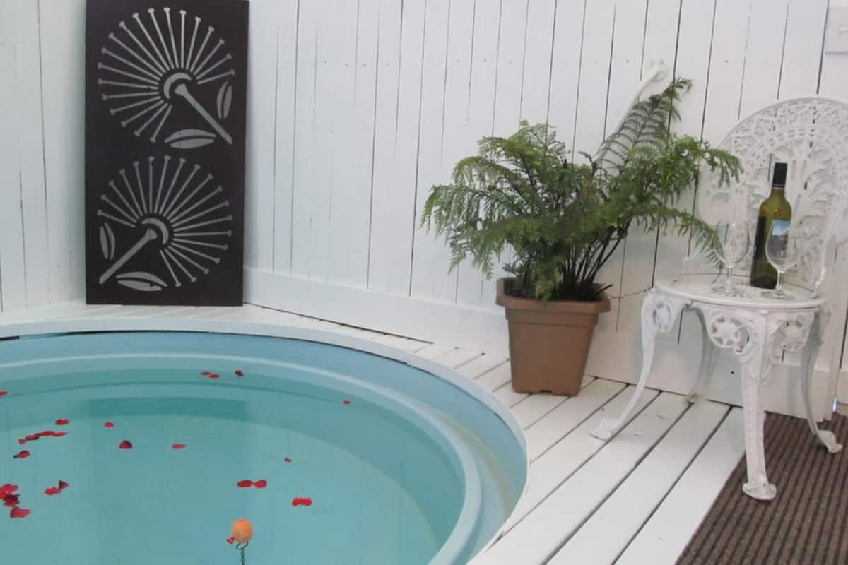 A pool area with a white wooden deck, a potted plant, and a white table with a bottle.