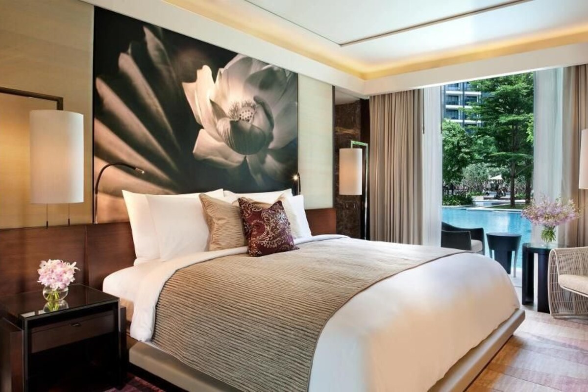 A hotel room with a large bed, a view of a swimming pool, and a lounge area with a chair.