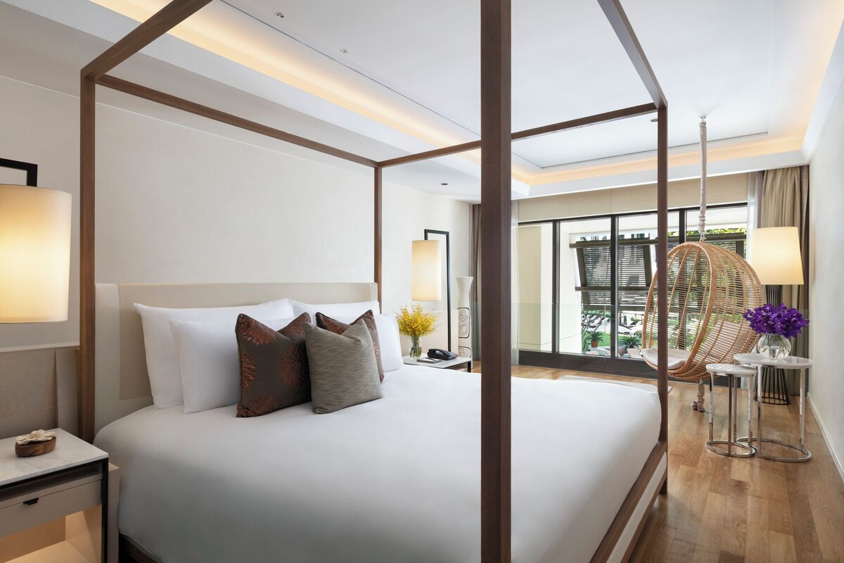 Una habitación de hotel moderna con cama a dosel, una zona de estar con una silla y vistas al exterior.