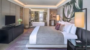A modern hotel room with a large bed, a television, a desk, and a bathroom visible through a glass door. - Siam Kempinski (Bangkok)