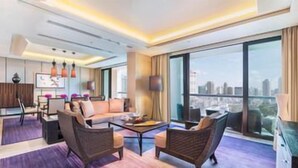 A modern hotel room with a large window, a sofa, a coffee table, and a TV. - Siam Kempinski (Bangkok)