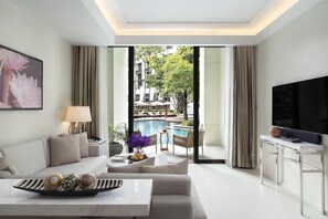 A modern hotel room with a sofa, a dining table, a TV, and a view of an outdoor swimming pool.