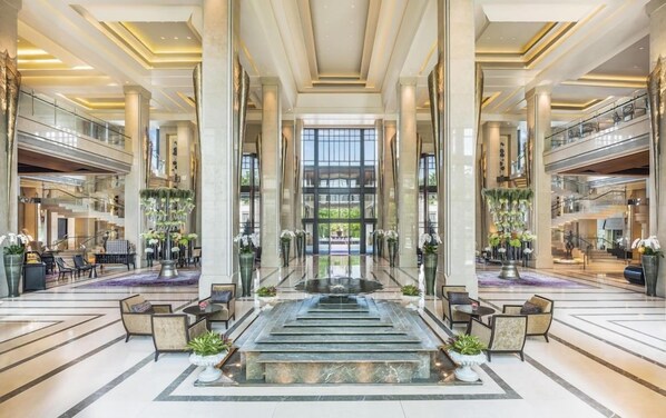 A spacious lobby with a central fountain, multiple seating areas, and a grand staircase.