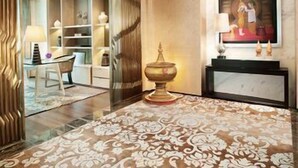 A room with a chandelier, a patterned carpet, a desk with a lamp, and a painting on the wall. - Siam Kempinski (Bangkok)