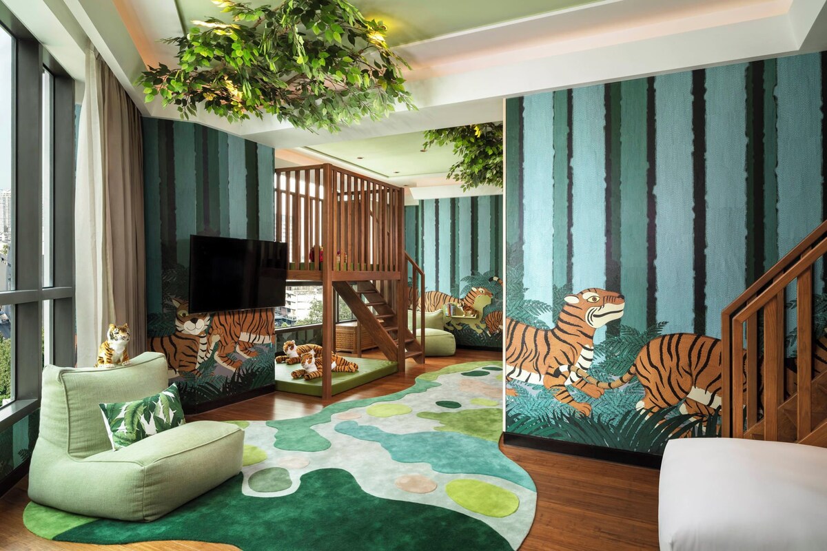 Una habitación con un ventanal grande, un sofá verde, una escalera de madera y un mural con temática de tigre.