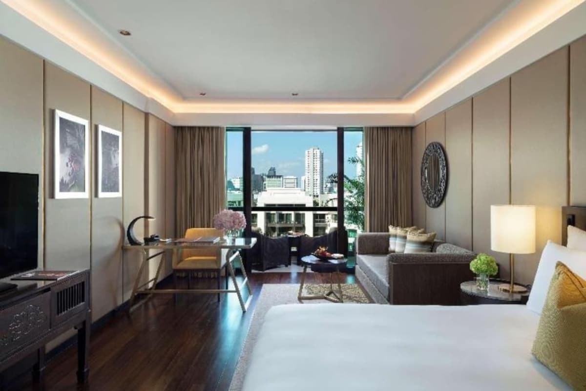 Habitación de hotel con una cama grande, un escritorio, una silla, un sofá, un televisor y vistas de la ciudad.