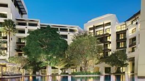 A swimming pool surrounded by modern buildings with balconies, trees, and a clear sky. - Siam Kempinski (Bangkok)