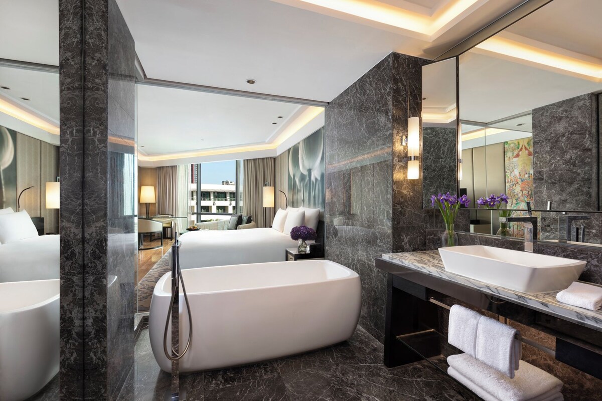 Habitación de hotel moderna con una bañera grande, zona de ducha separada, un espejo amplio y vistas a la ciudad.